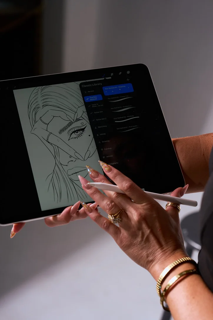 Taylor holding her iPad with The Star Method brush library open beside a line drawing, Apple Pencil in hand